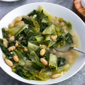 A shallow bowl of brothy escarole and beans with a soup spoon.