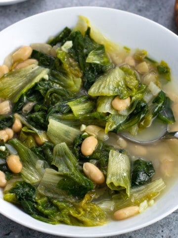 A shallow bowl of brothy escarole and beans with a soup spoon.