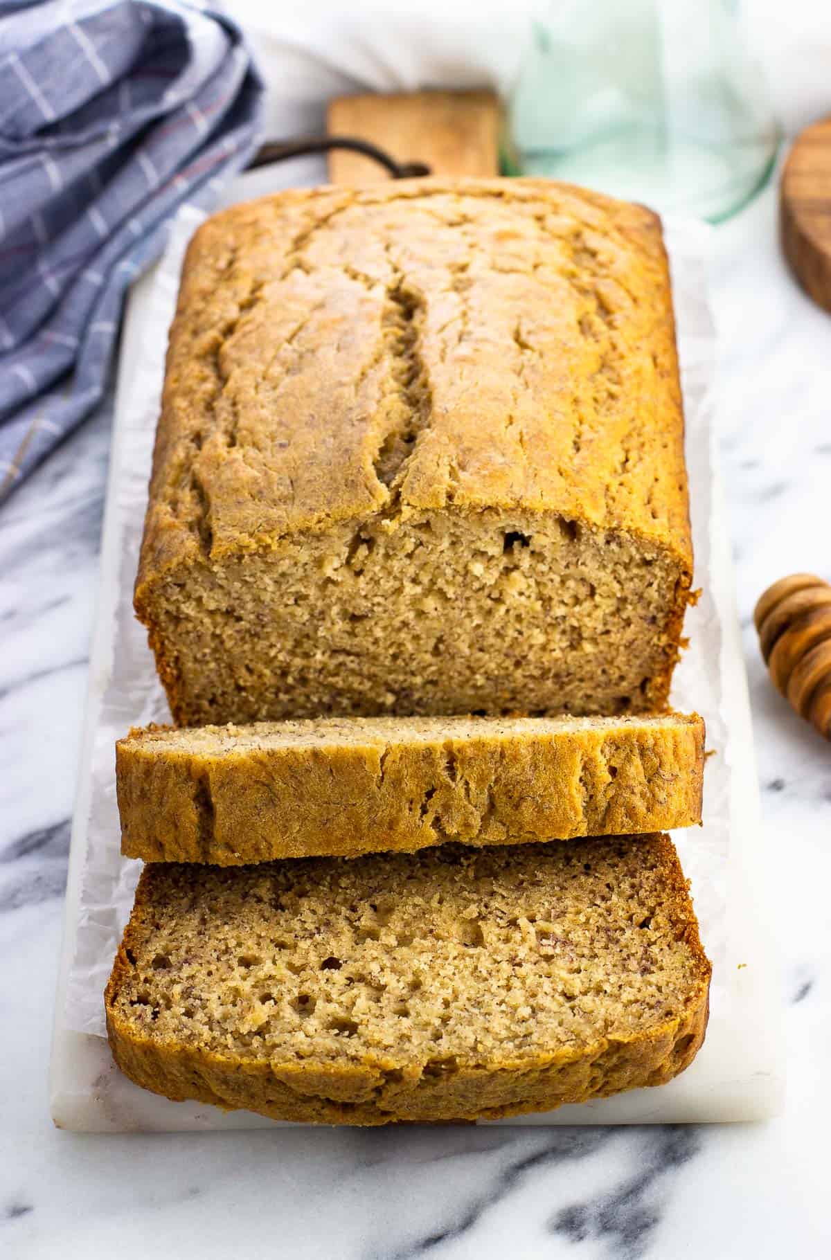 A half-sliced loaf of honey banana bread on a marble serving board.