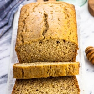 A half-sliced loaf of honey banana bread on a marble serving board.