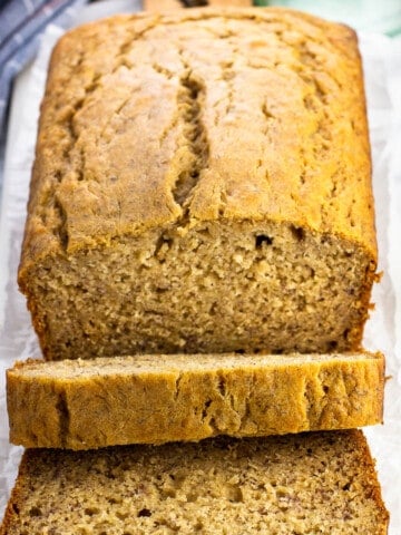 A half-sliced loaf of honey banana bread on a marble serving board.