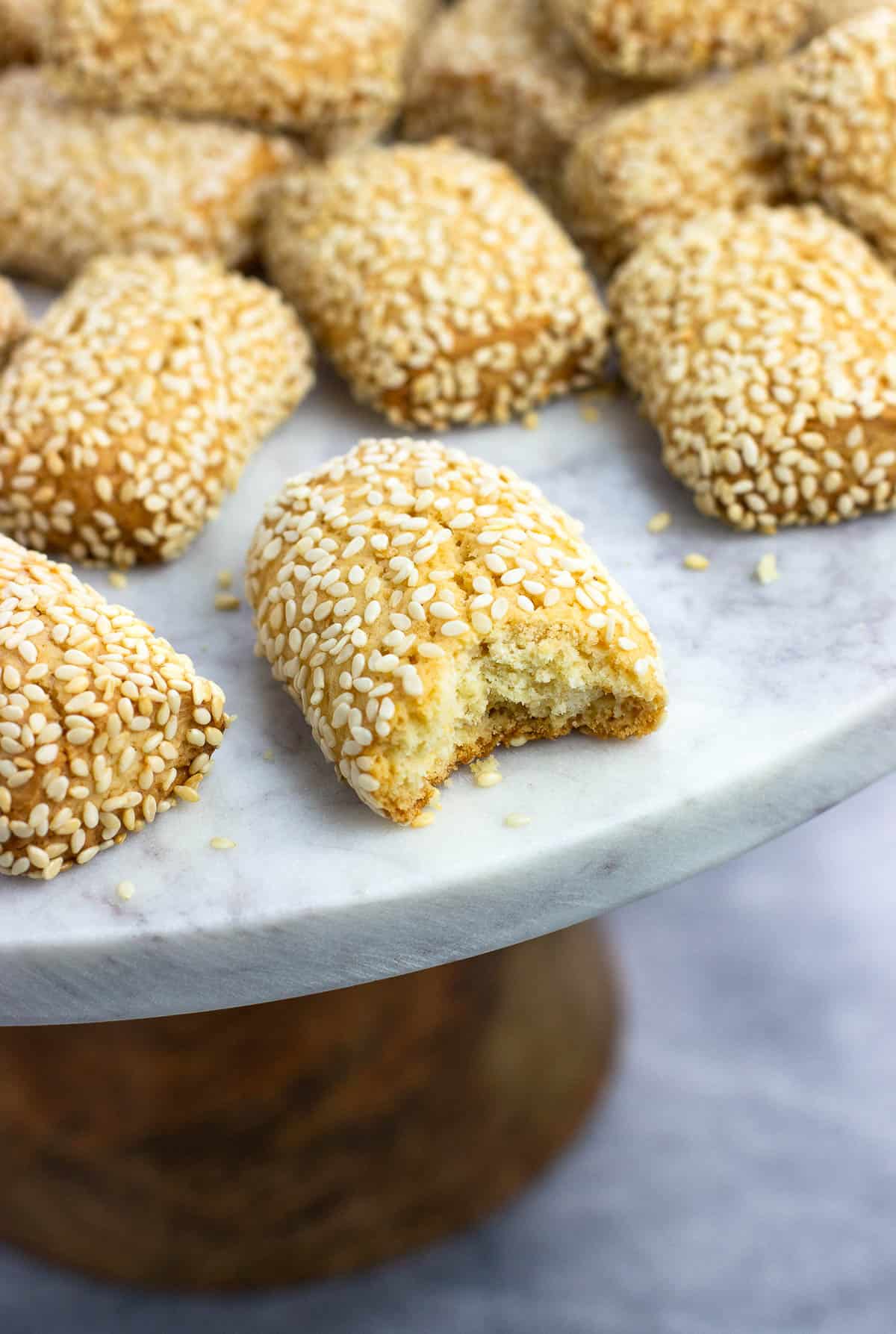 A sesame seed cookie on a serving plate with a bite taken out of it.