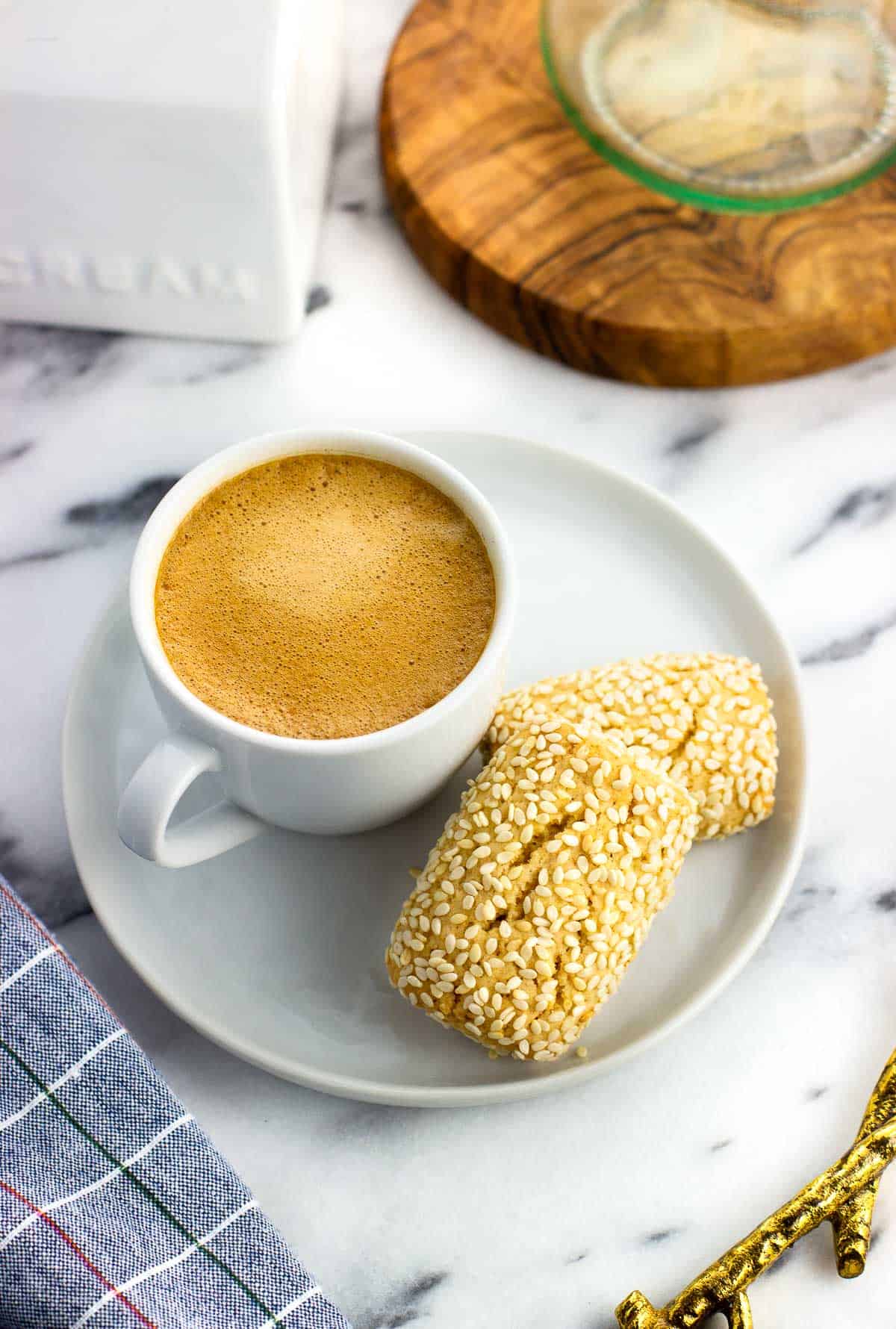 Two sesame cookies on a small plate next to a demitasse cup filled with espresso.