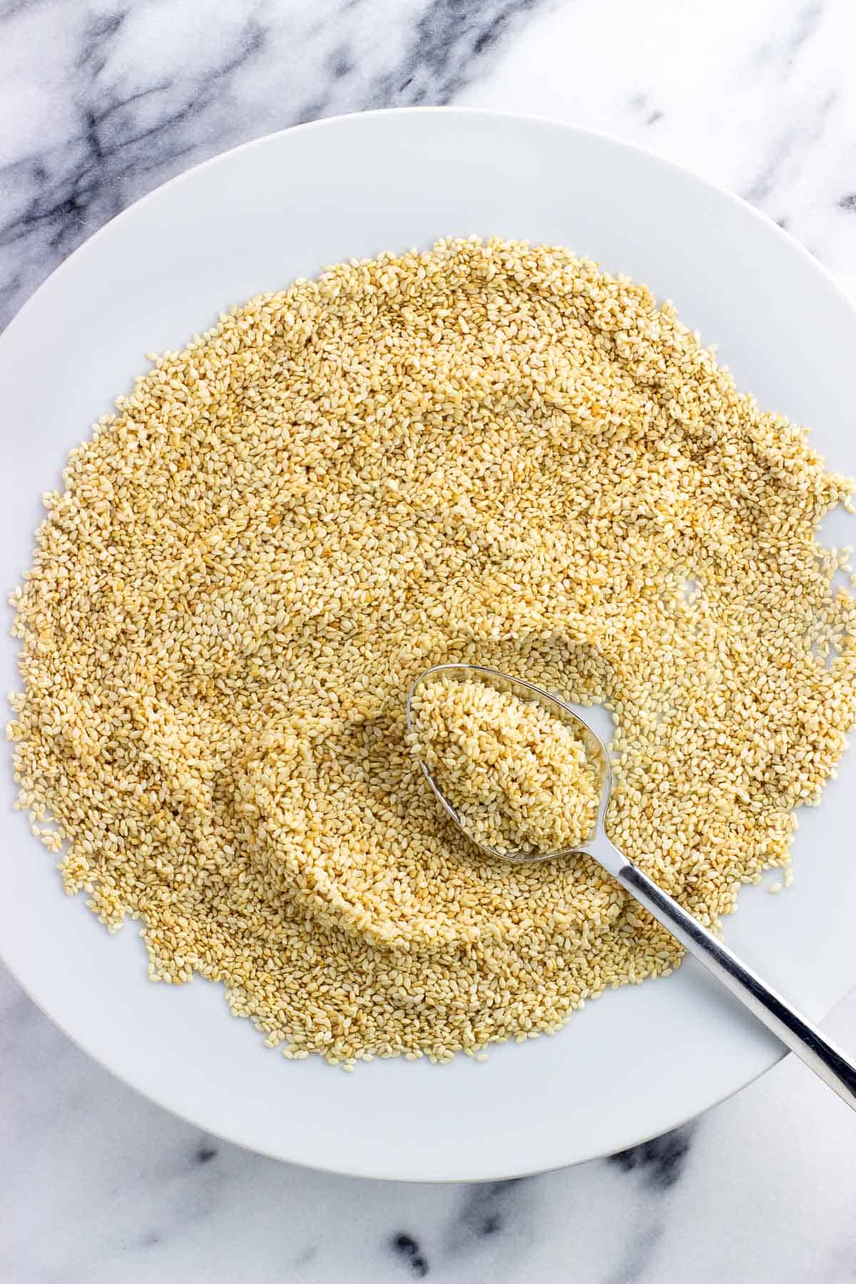 A spoon in a plate of toasted sesame seeds.