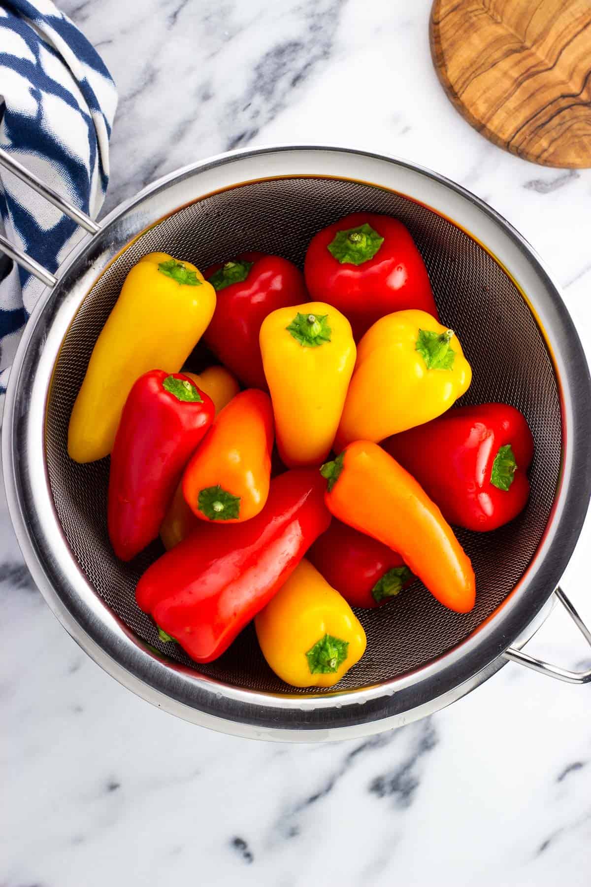 Twelve mini sweet peppers in a large strainer.