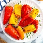 Roasted mini peppers on a serve plate garnished with fresh herbs.