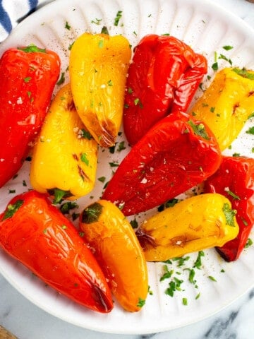 Roasted mini peppers on a serve plate garnished with fresh herbs.