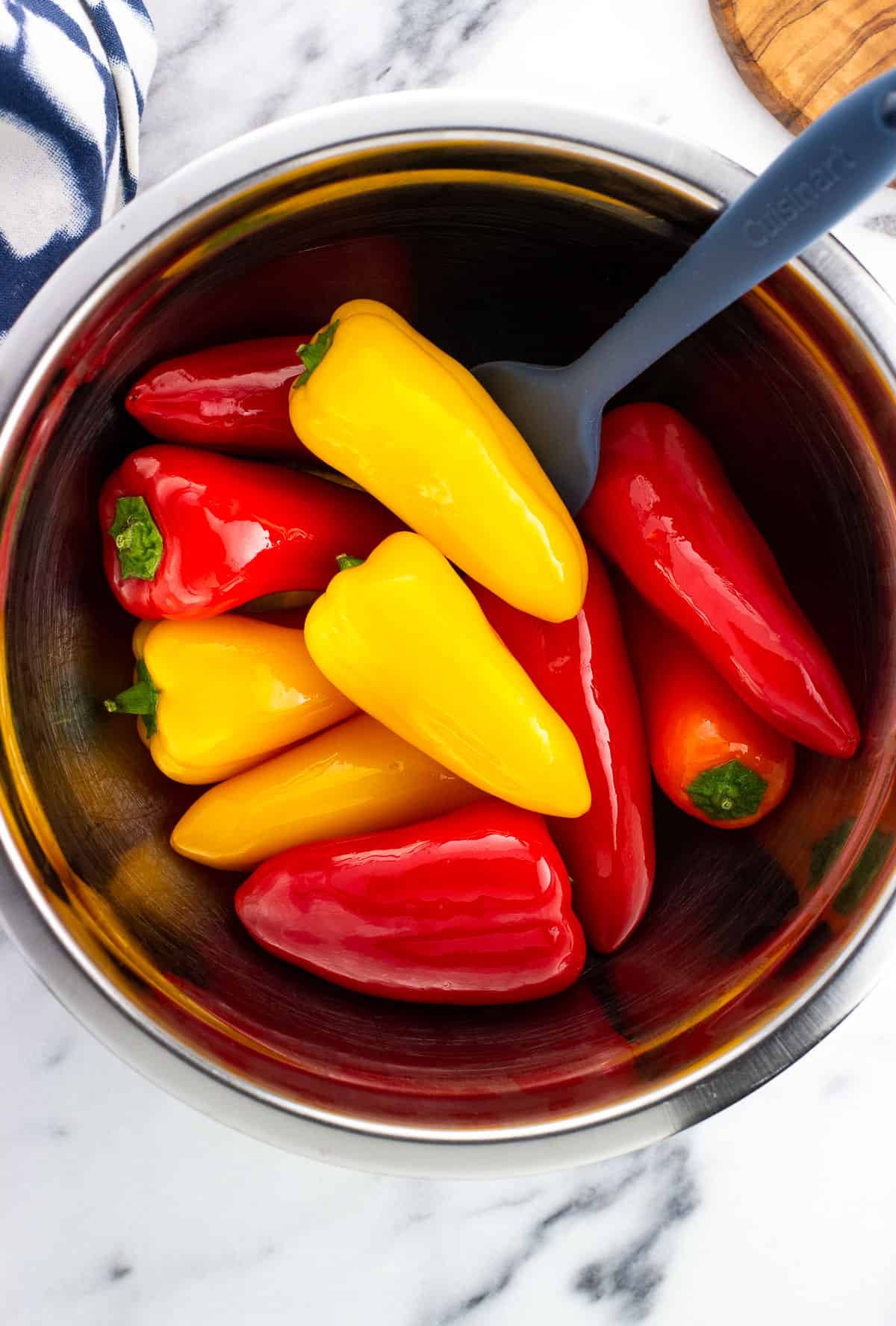 Whole mini peppers and a spatula in a mixing bowl tossing the peppers with olive oil.