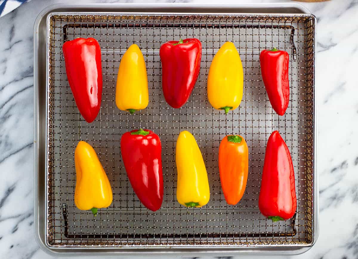 Oil-rubbed whole mini peppers on a mesh air fryer tray.