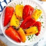 Roasted mini peppers on a serve plate garnished with fresh herbs.