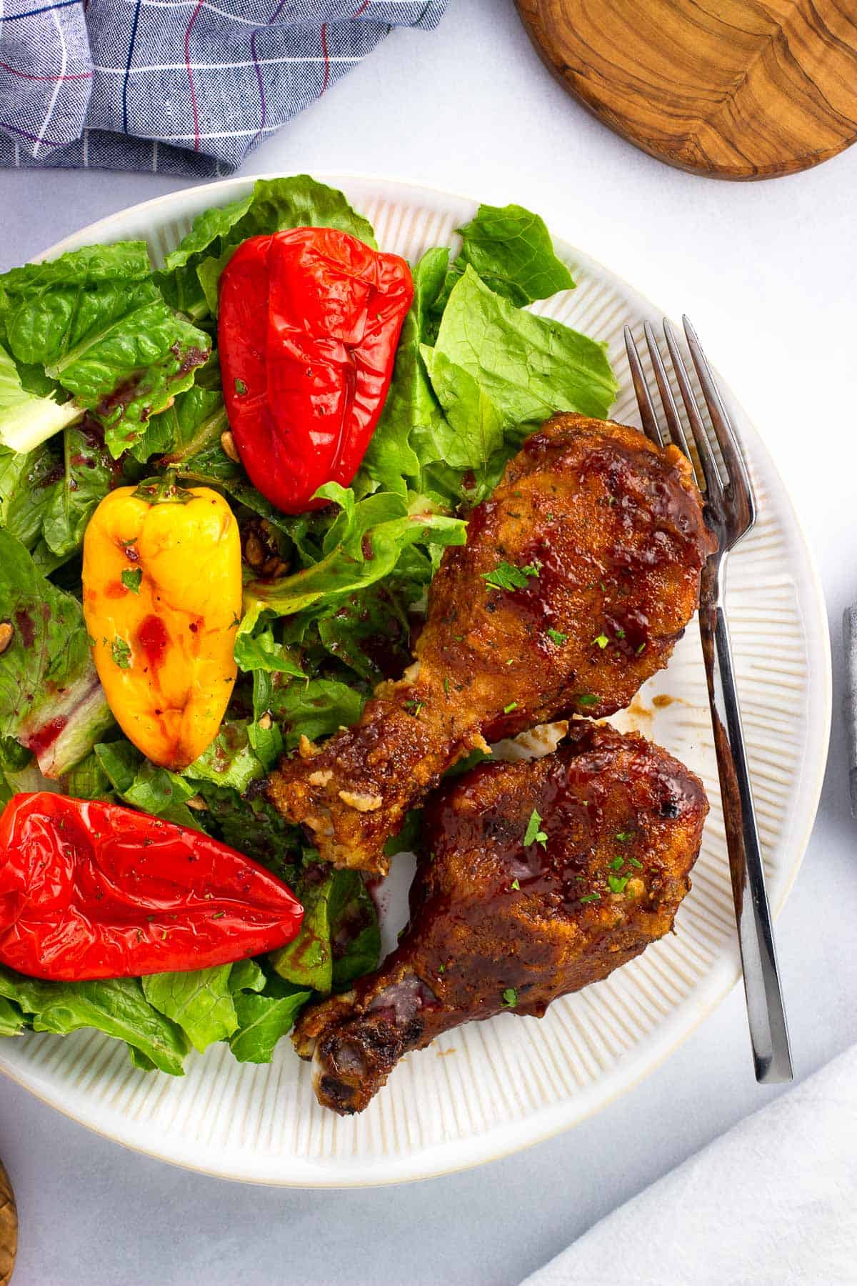 Two chicken drumsticks on a plate with a salad and a fork.