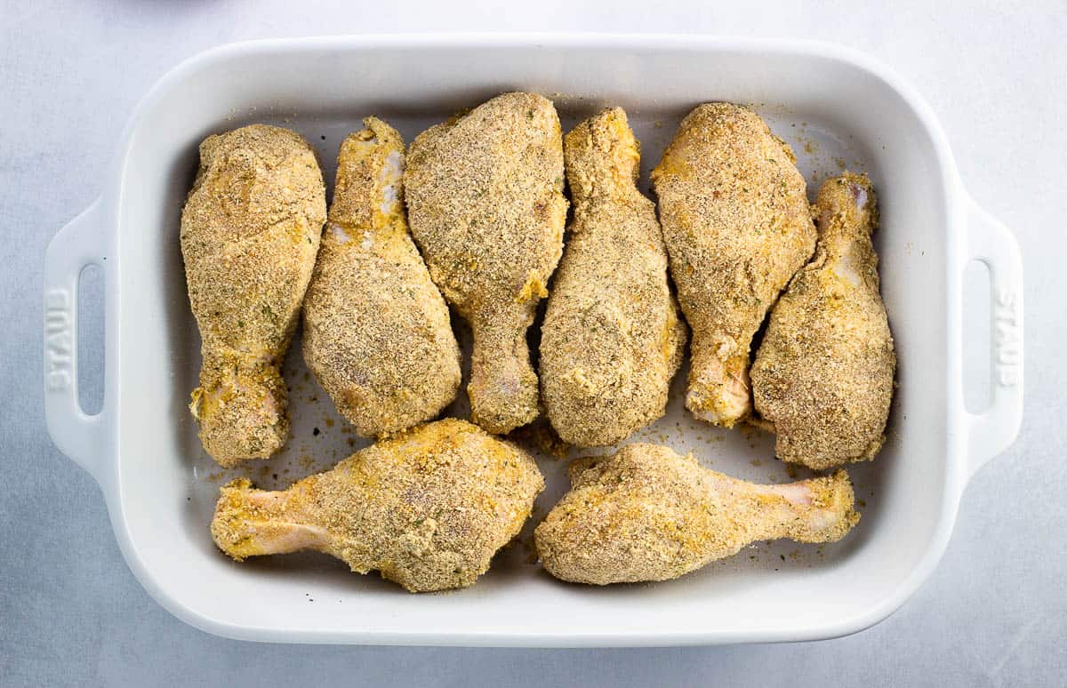 Breaded chicken drumsticks in a pan partway baked.