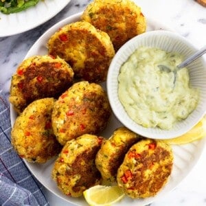 Eight salmon patties on a plate with a bowl of tartar sauce and lemon wedges.