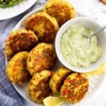 Salmon patties on a serving plate with a bowl of tartar sauce and lemon wedges.