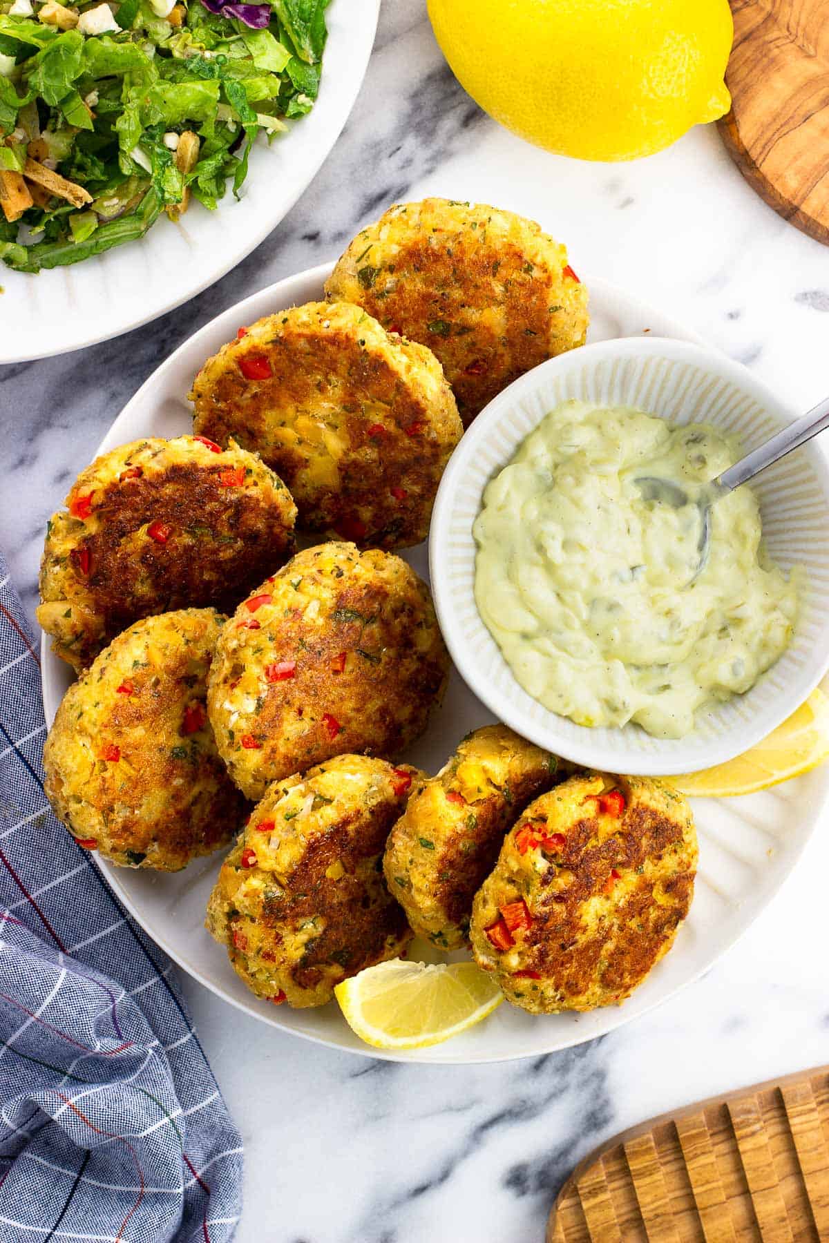 Salmon patties on a serving plate with a bowl of tartar sauce and lemon wedges.