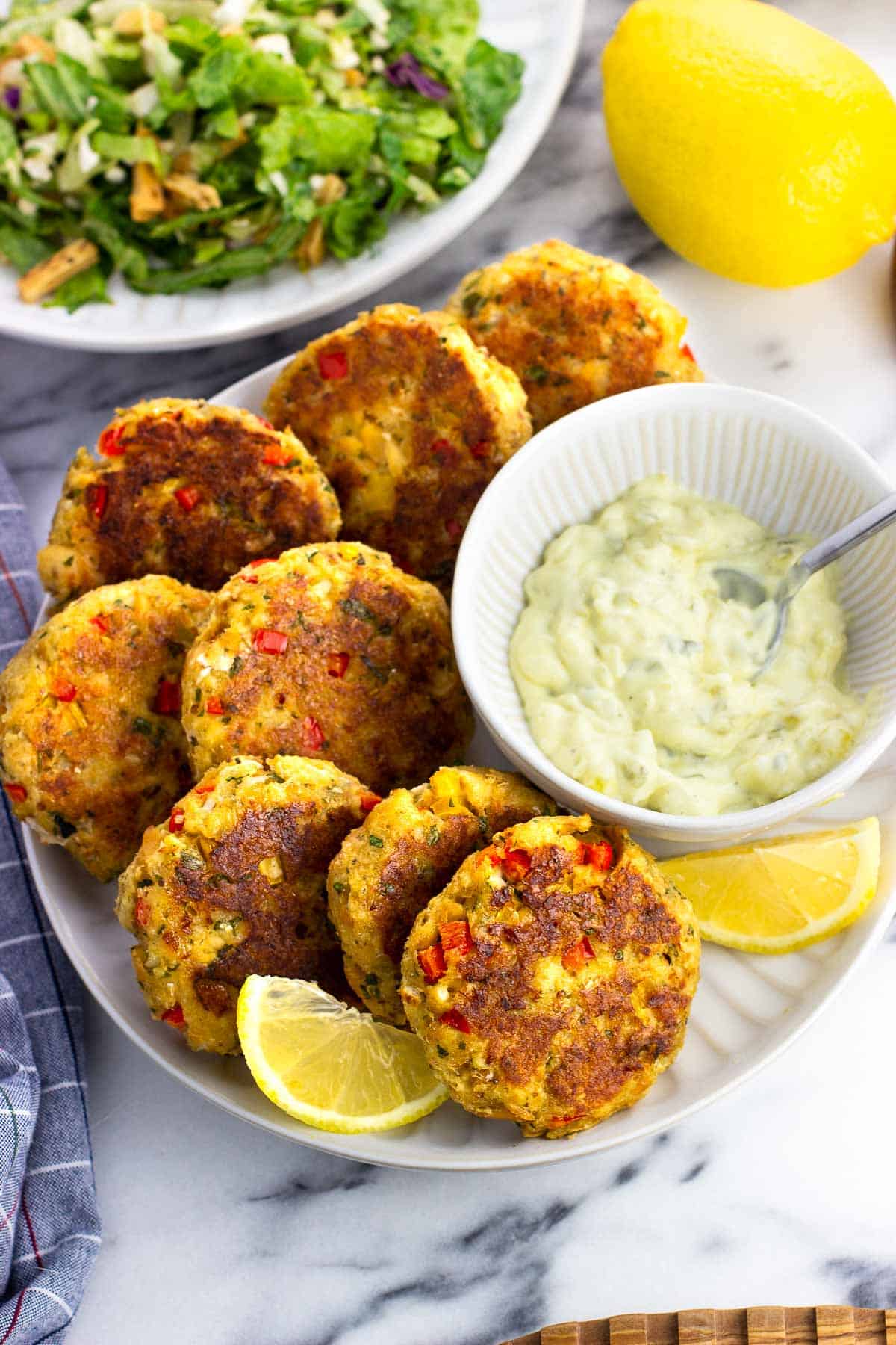 Eight salmon patties on a plate with a bowl of tartar sauce and lemon wedges.