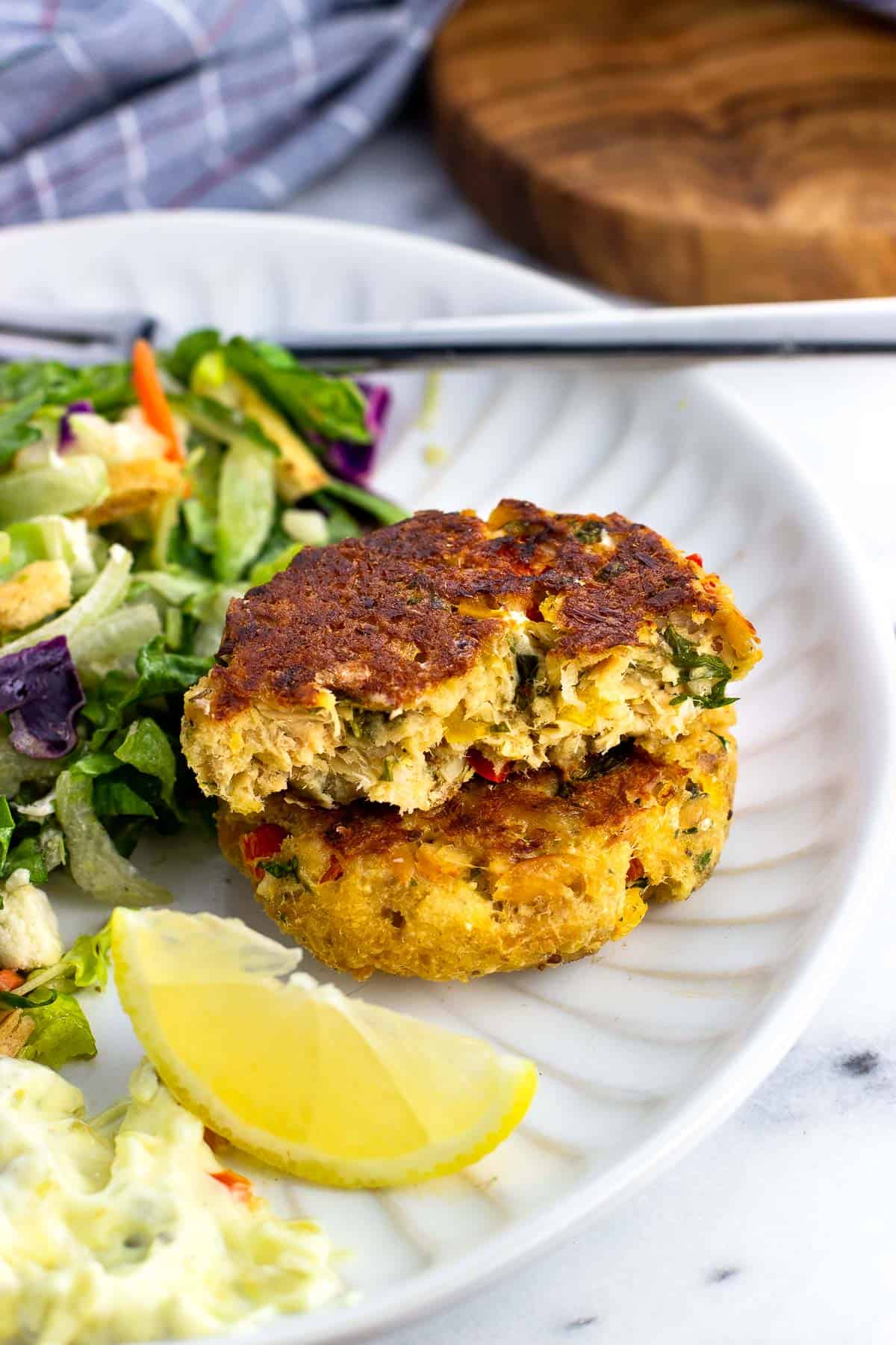 A plate of salad and two salmon patties stacked on each other, the top one cut in half.