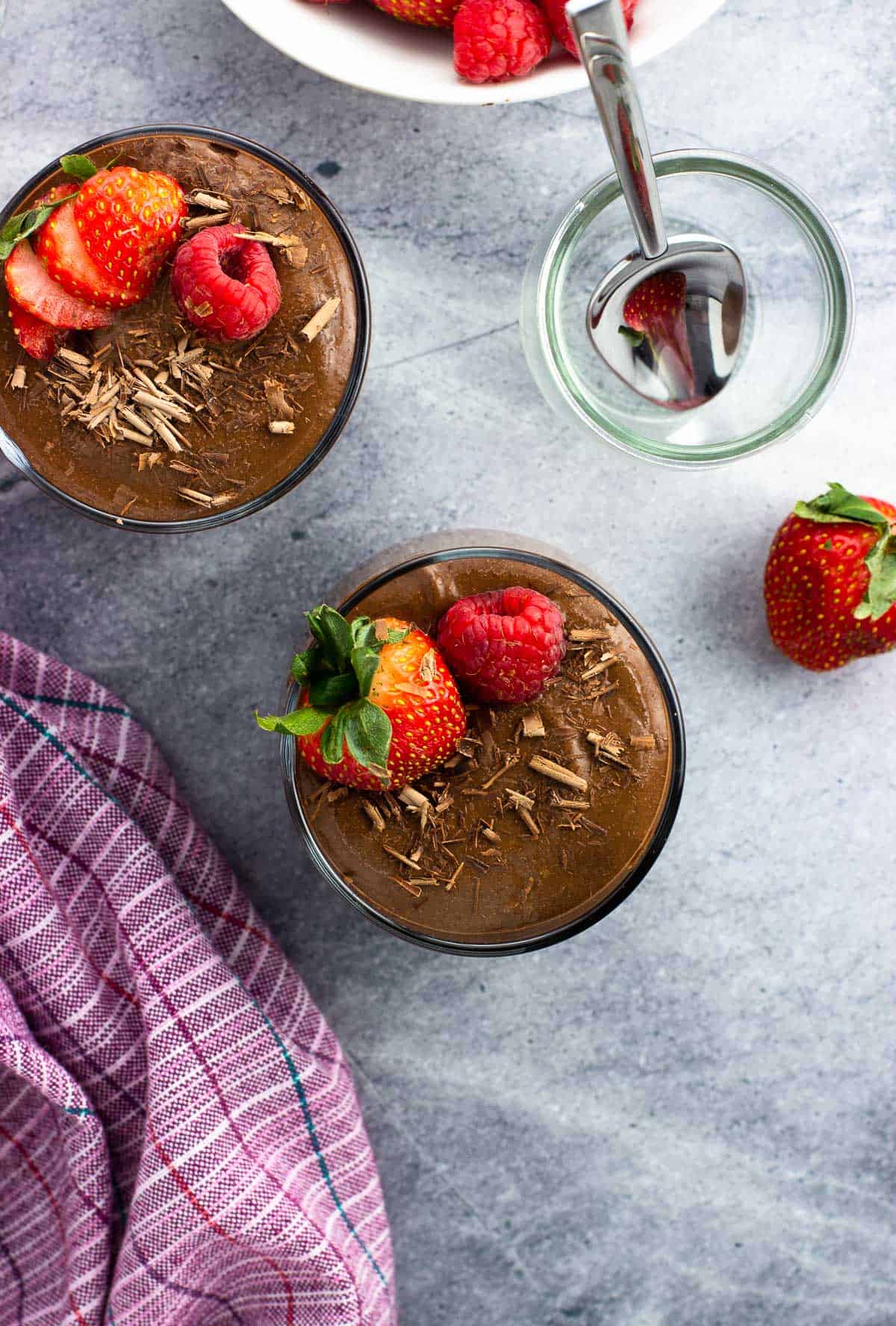Two cups of chocolate chia pudding topped with chocolate shavings and fruit.