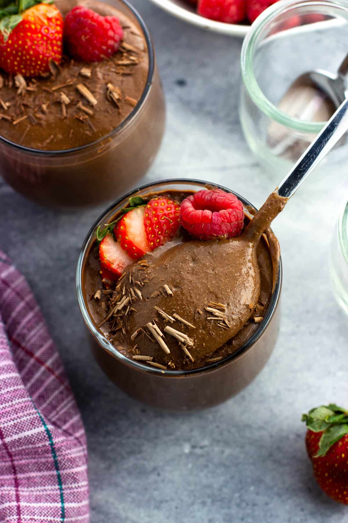 A spoon lifting out of a cup of blended chocolate chia pudding.