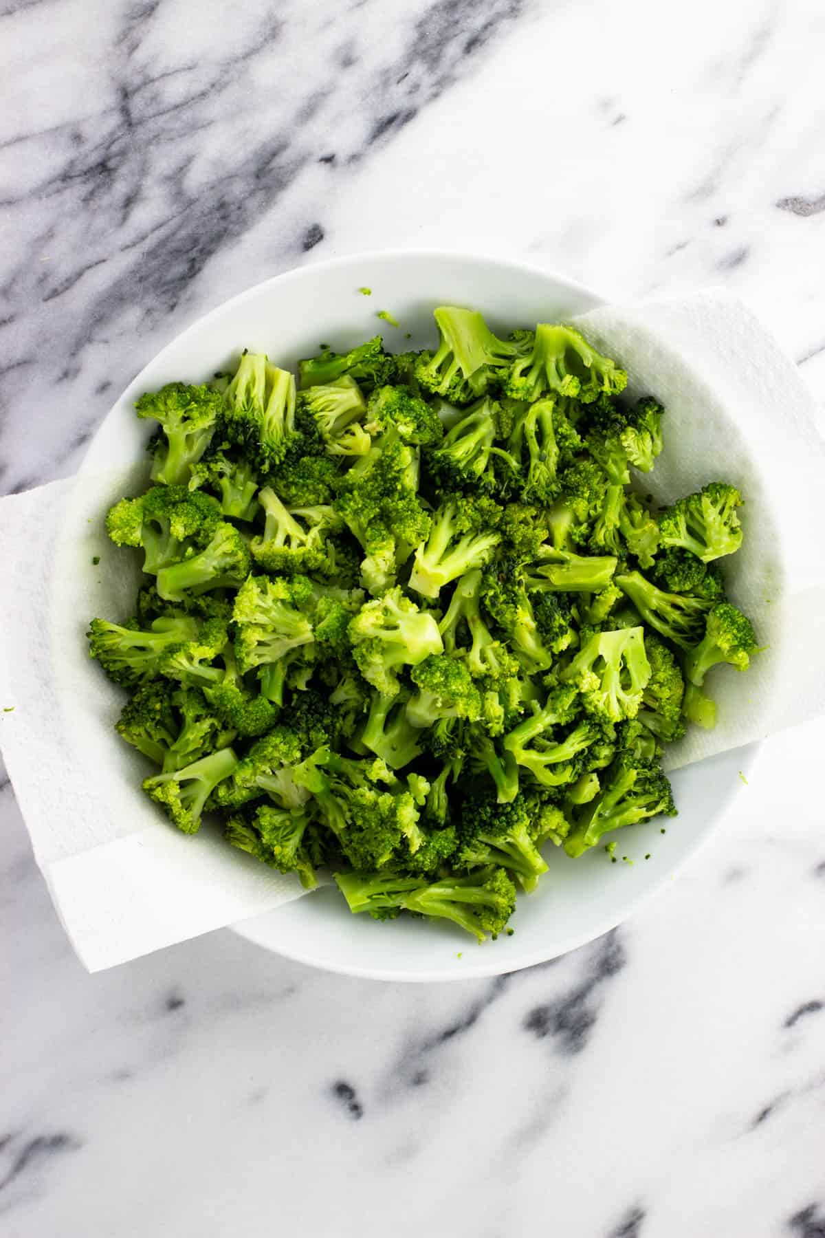 Steamed broccoli florets in a paper towel-lined shallow bowl.