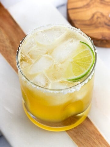 A short salt-rimmed glass of a margarita mocktail garnished with a lime wedge.