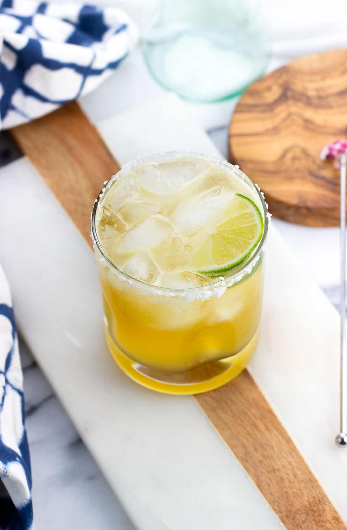 A short salt-rimmed glass of a margarita mocktail garnished with a lime wedge.