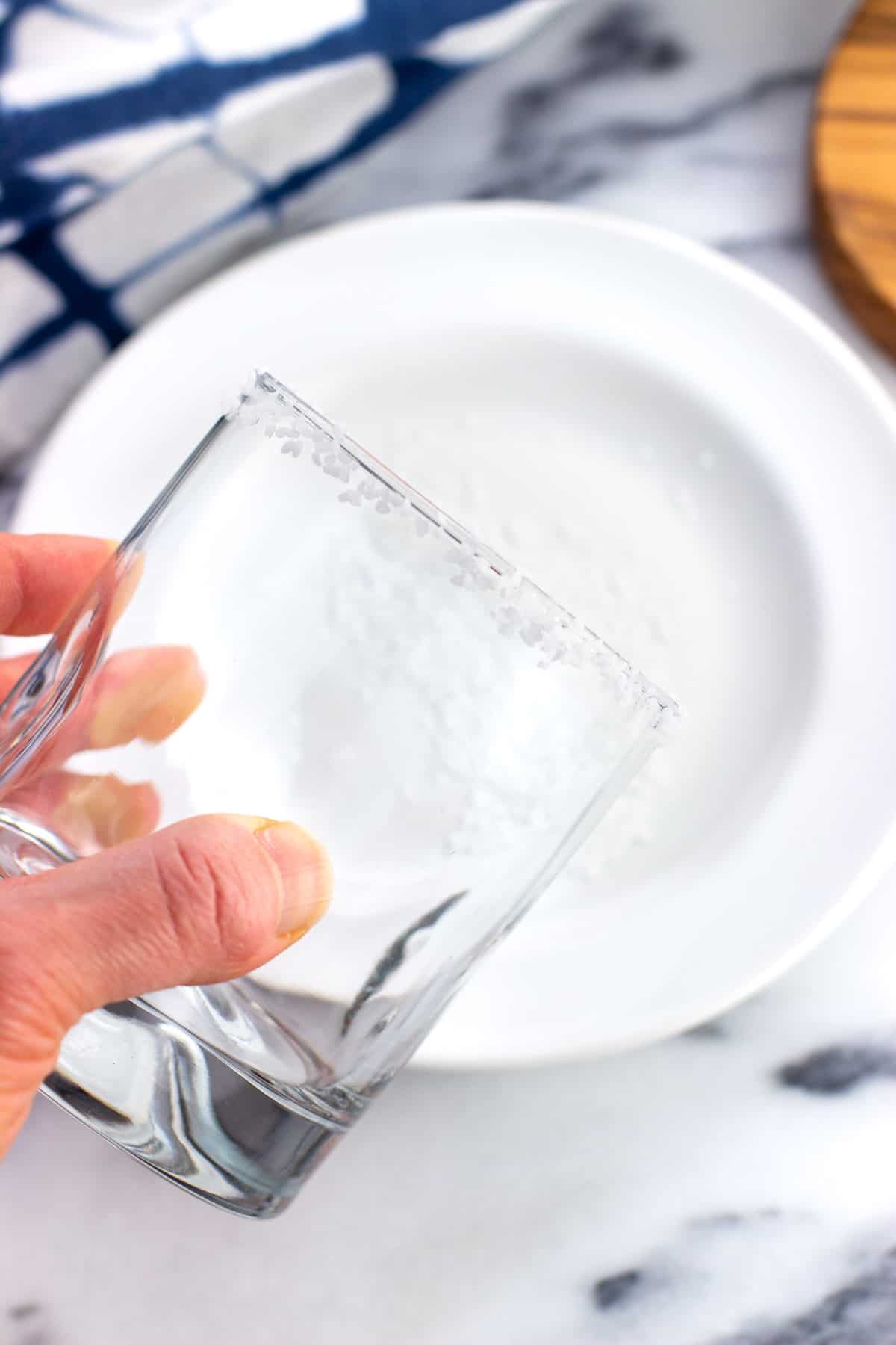 A hand rolling the rim of a short glass into a plate of coarse salt.
