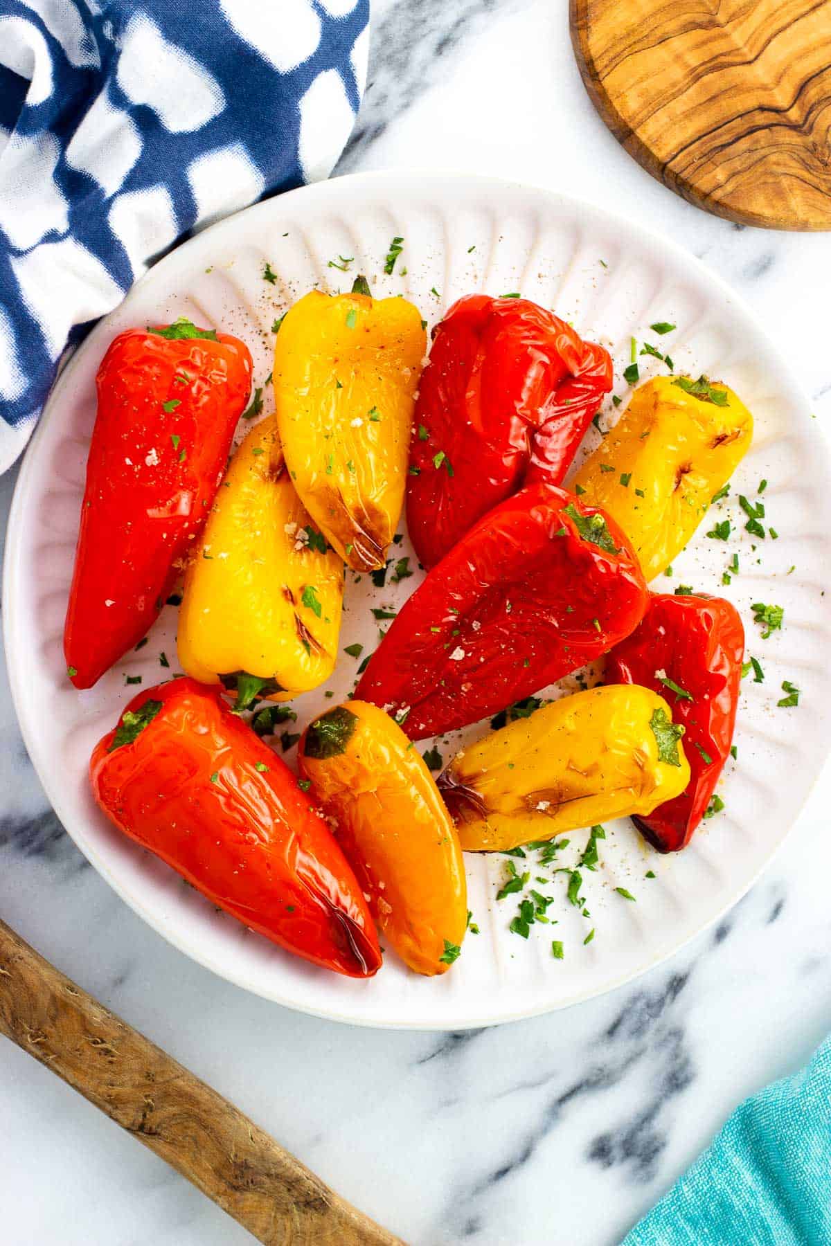Roasted mini peppers on a serve plate garnished with fresh herbs.