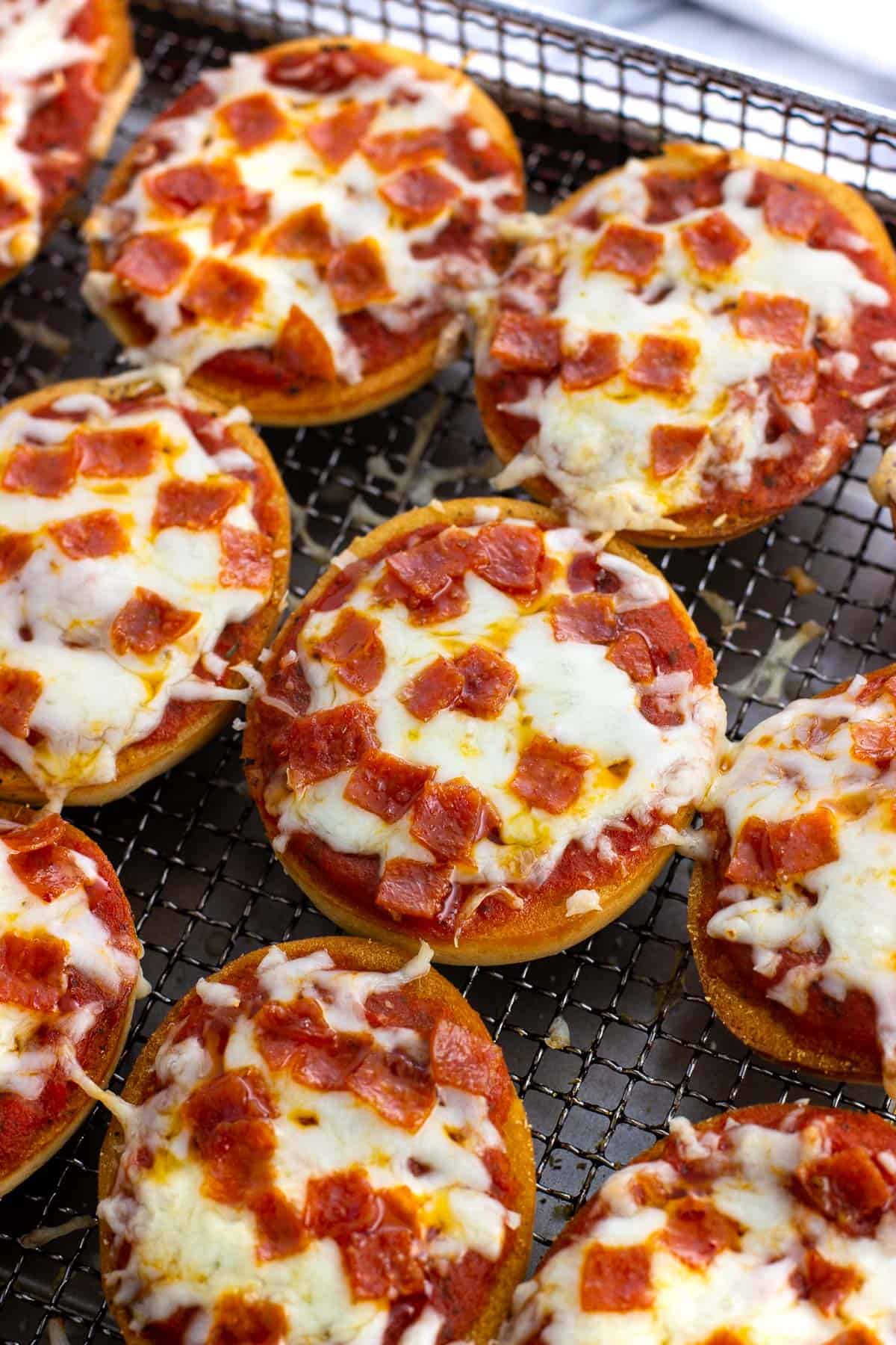 Cooked pizza bagels on a wire air fryer basket.