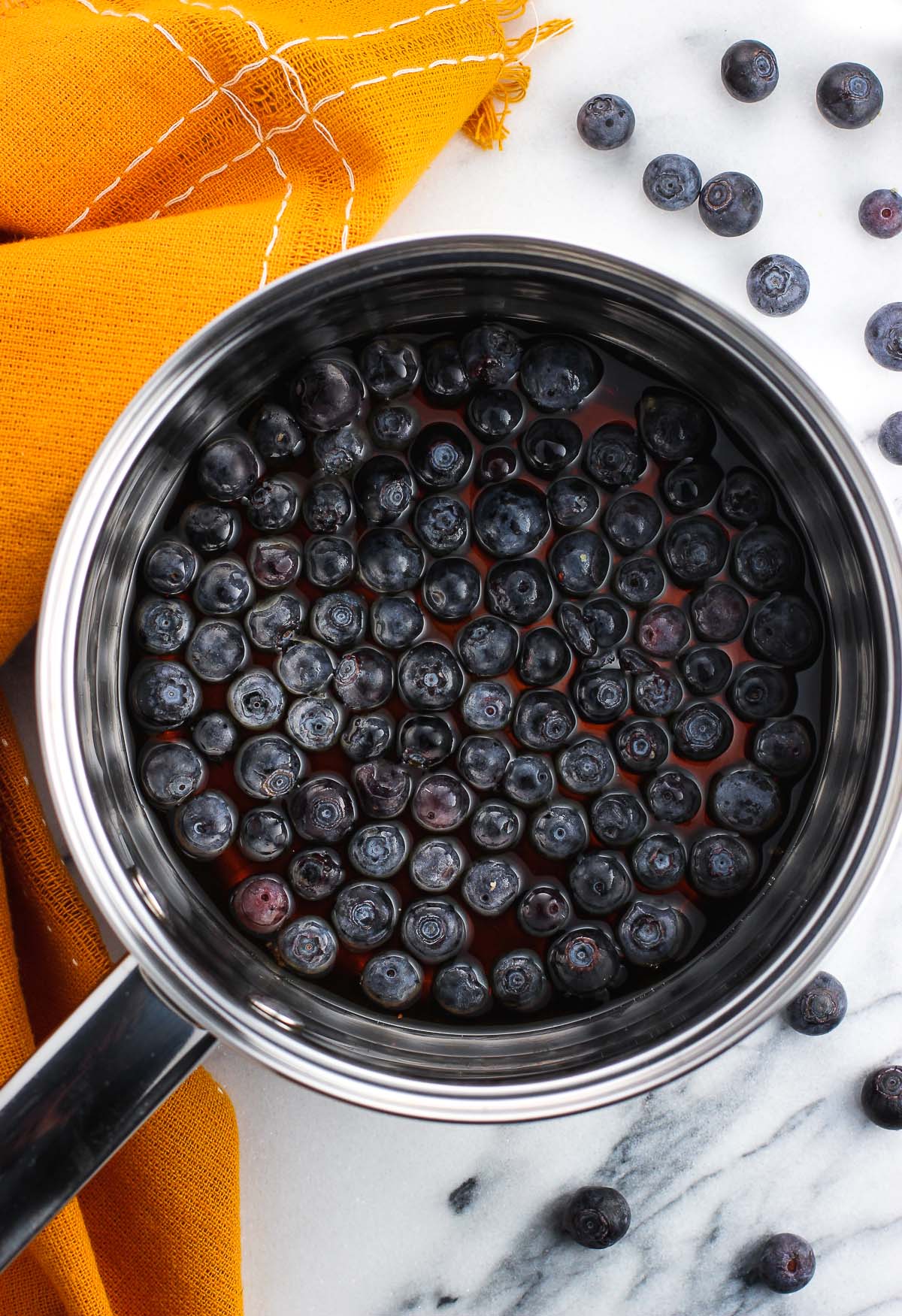 Whole blueberries in a saucepan of maple syrup.