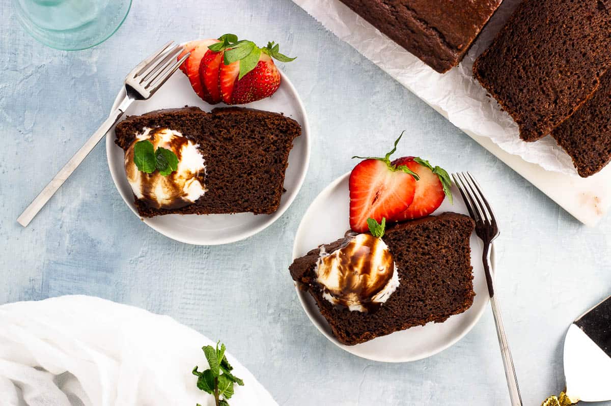 Two slices of chocolate yogurt cake on plates with scoops of ice cream and strawberries.