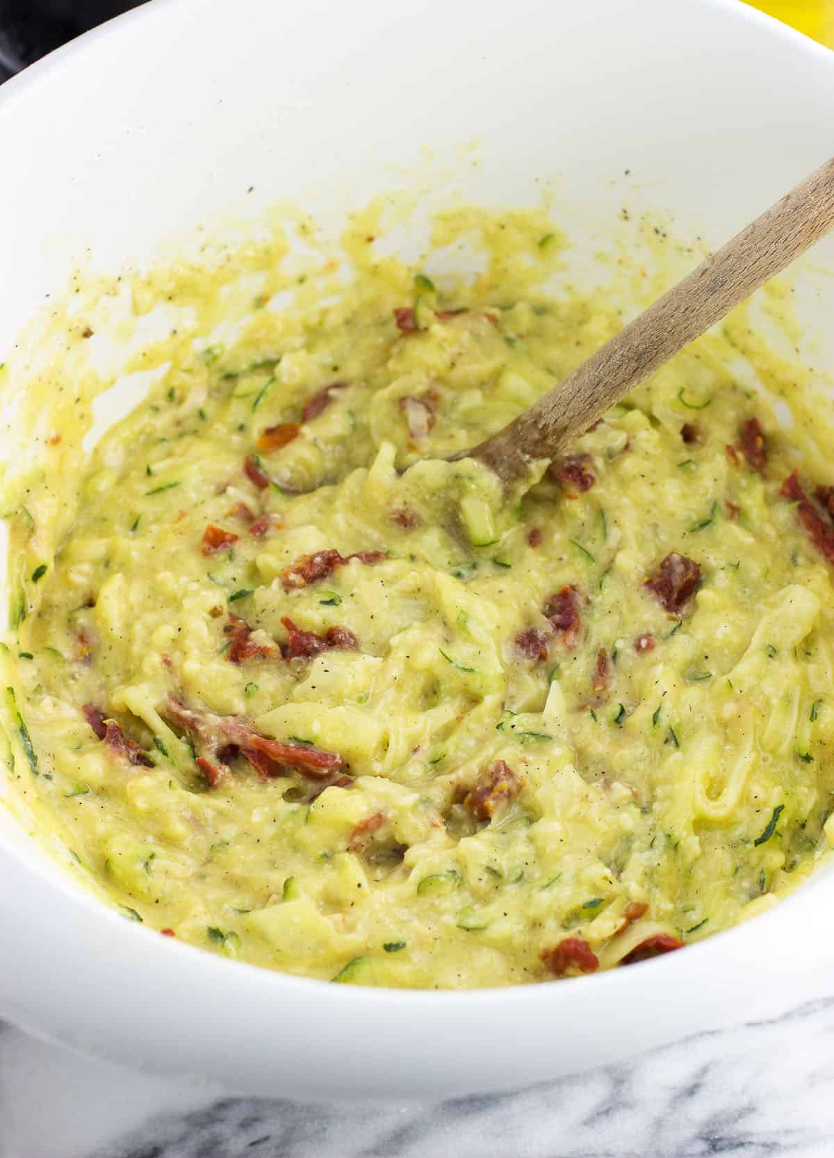 Combined zucchini pie mixture in a bowl with a wooden spoon.