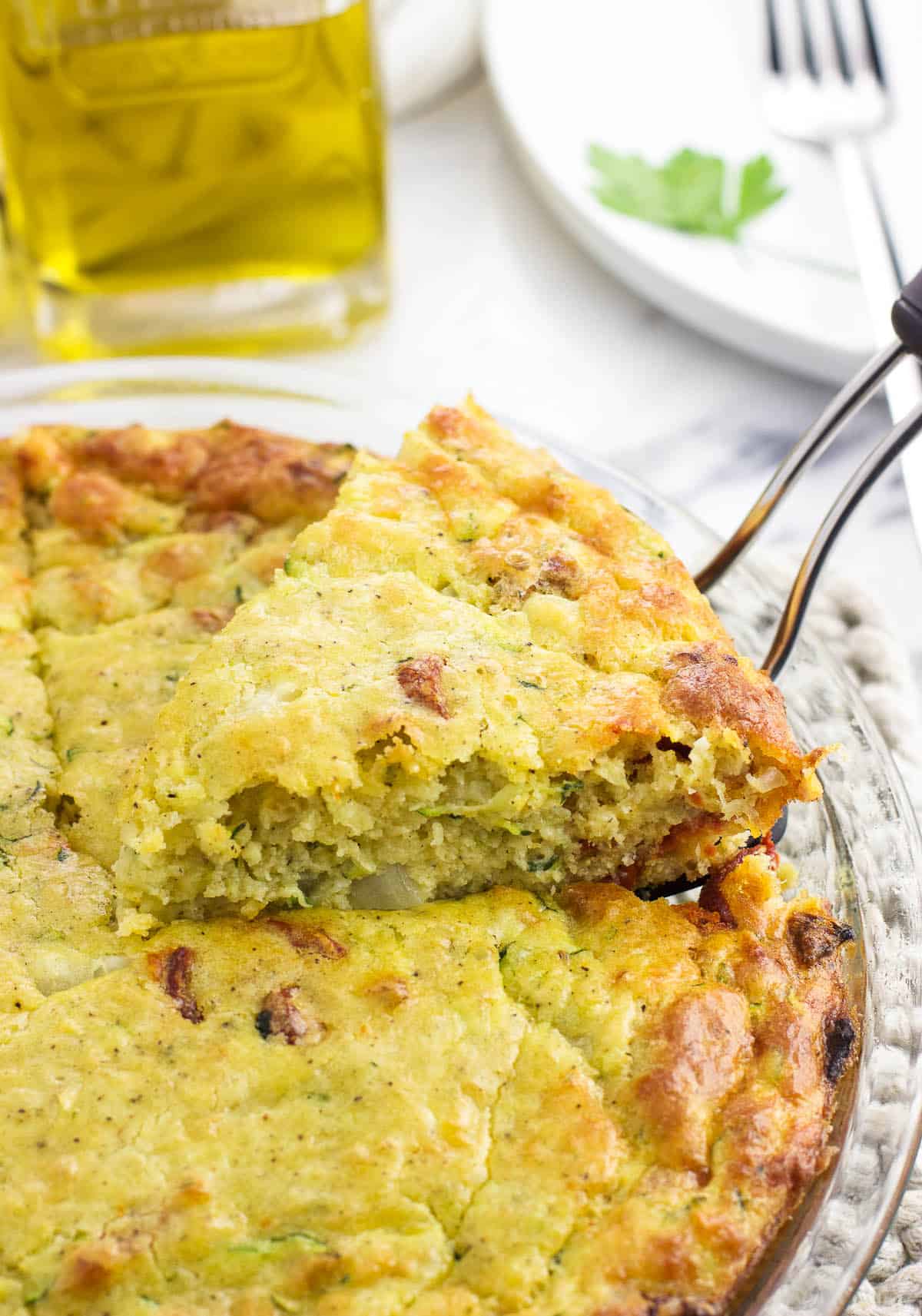 A wedge of zucchini pie being lifted out of the pan with a spatula.