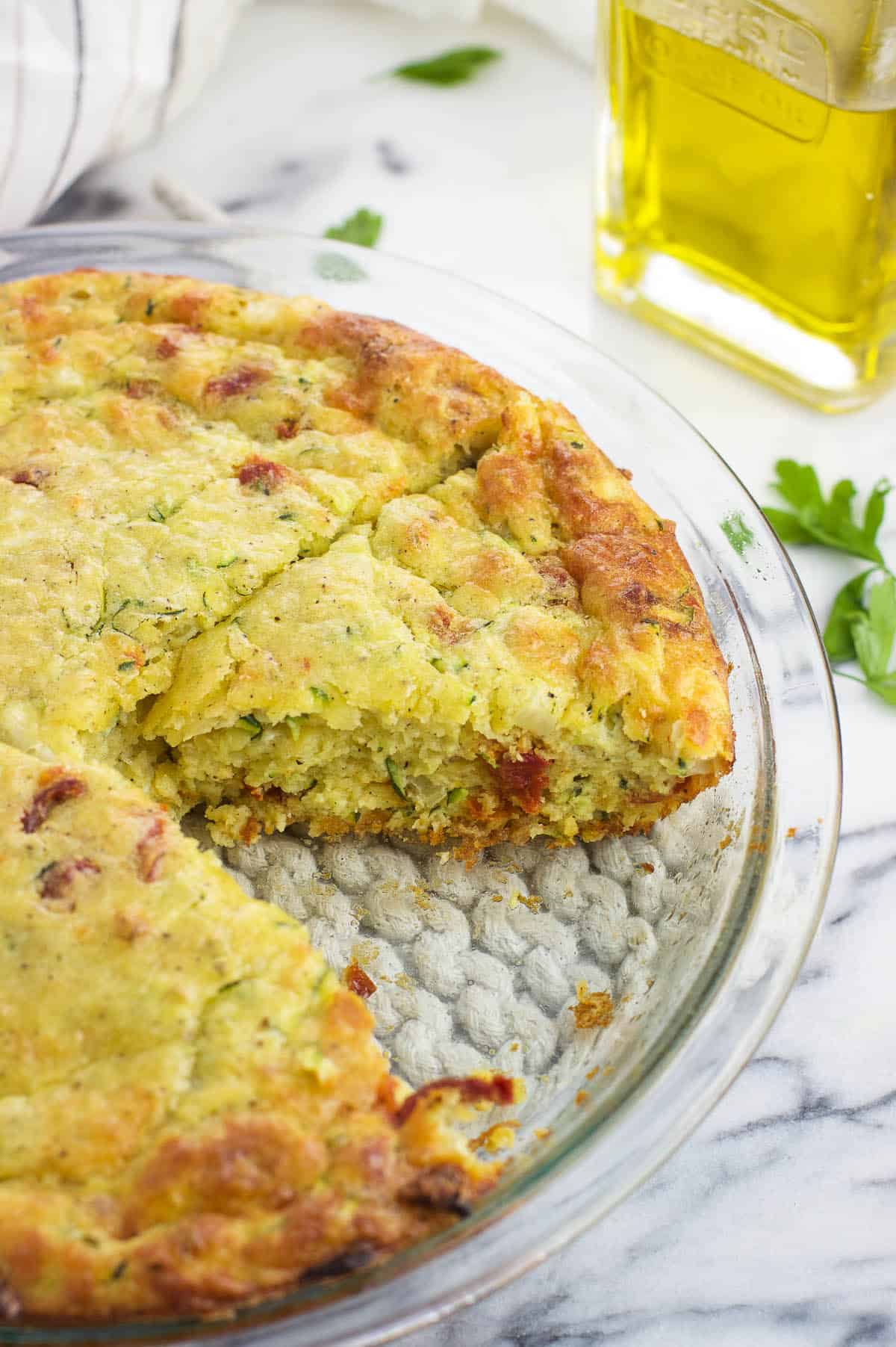 Partially-sliced zucchini pie in the glass pie plate with one wedge removed.