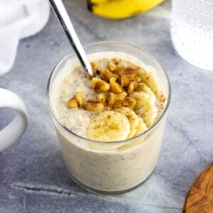 A short glass of protein overnight oats topped with walnuts and banana slices.