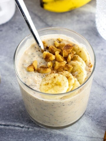 A short glass of protein overnight oats topped with walnuts and banana slices.