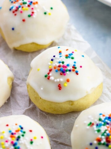 Glazed anginetti cookies on a crinkled sheet of parchment paper.