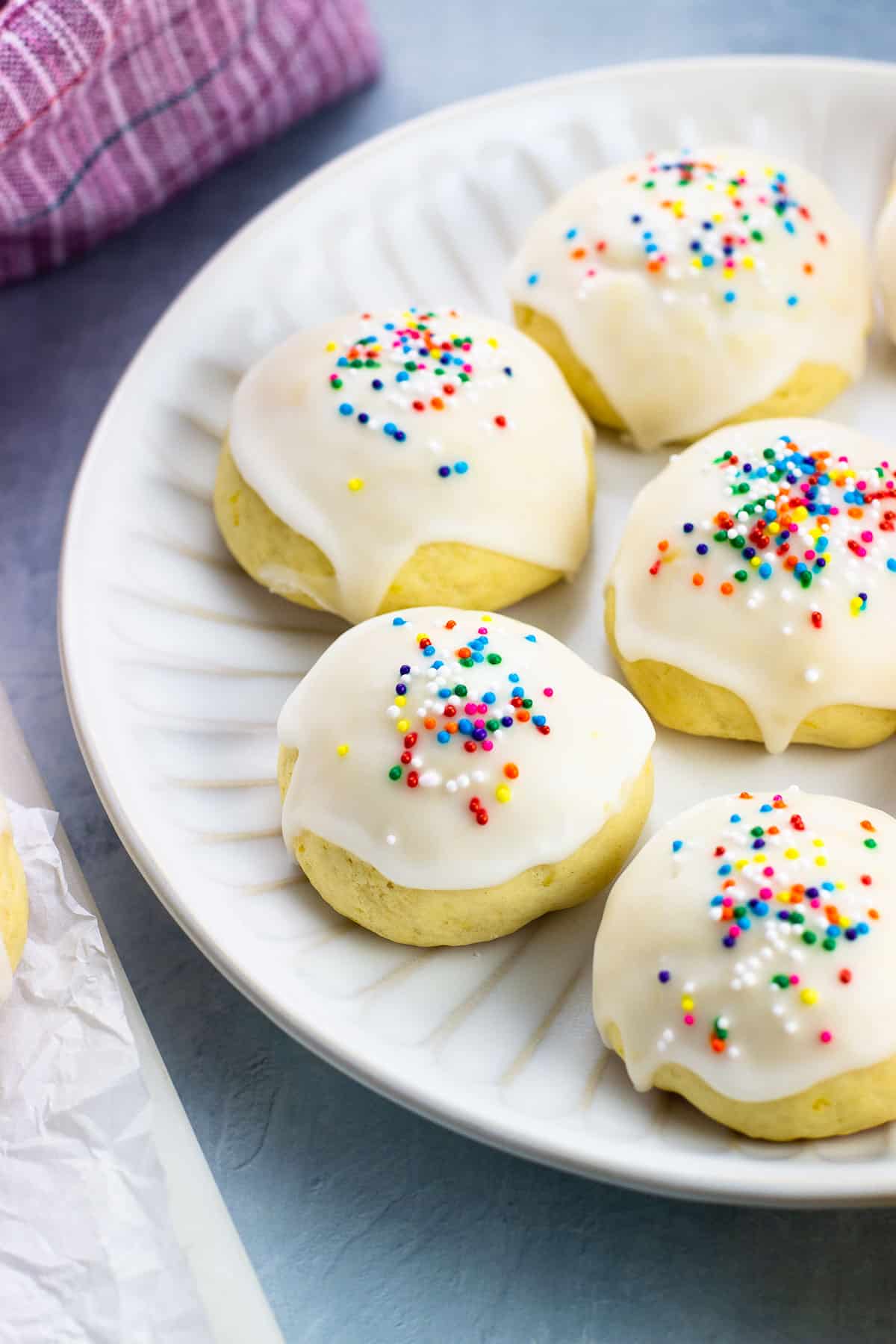 A plate of glazed Italian lemon drop cookies decorated with rainbow nonpareils.