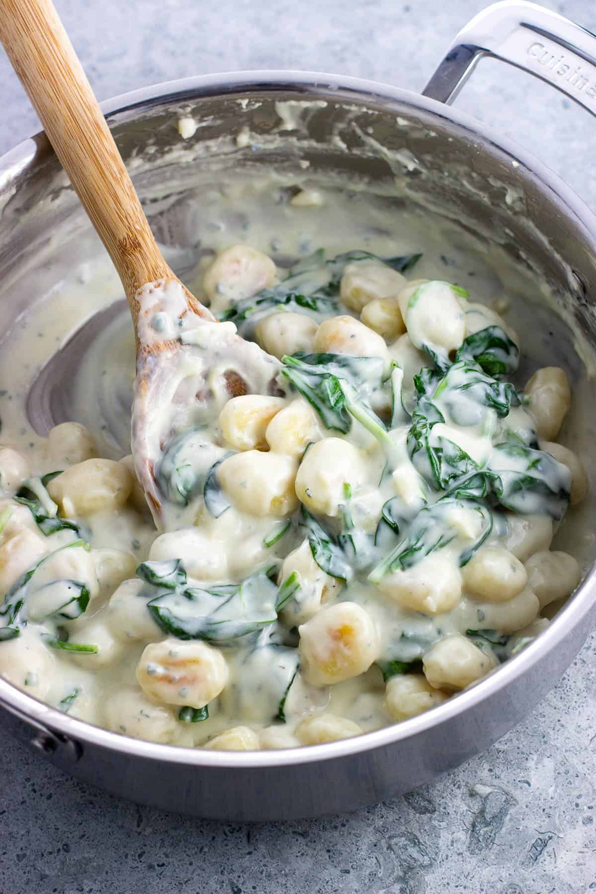 Gnocchi and spinach in a creamy Gorgonzola sauce in a stainless steel saucepan.