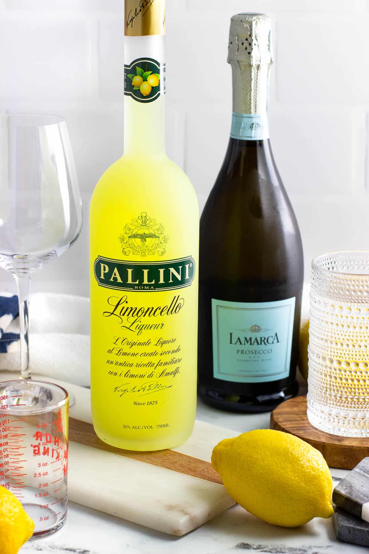 Bottles of prosecco and limoncello next to a measuring cup and fresh lemons.