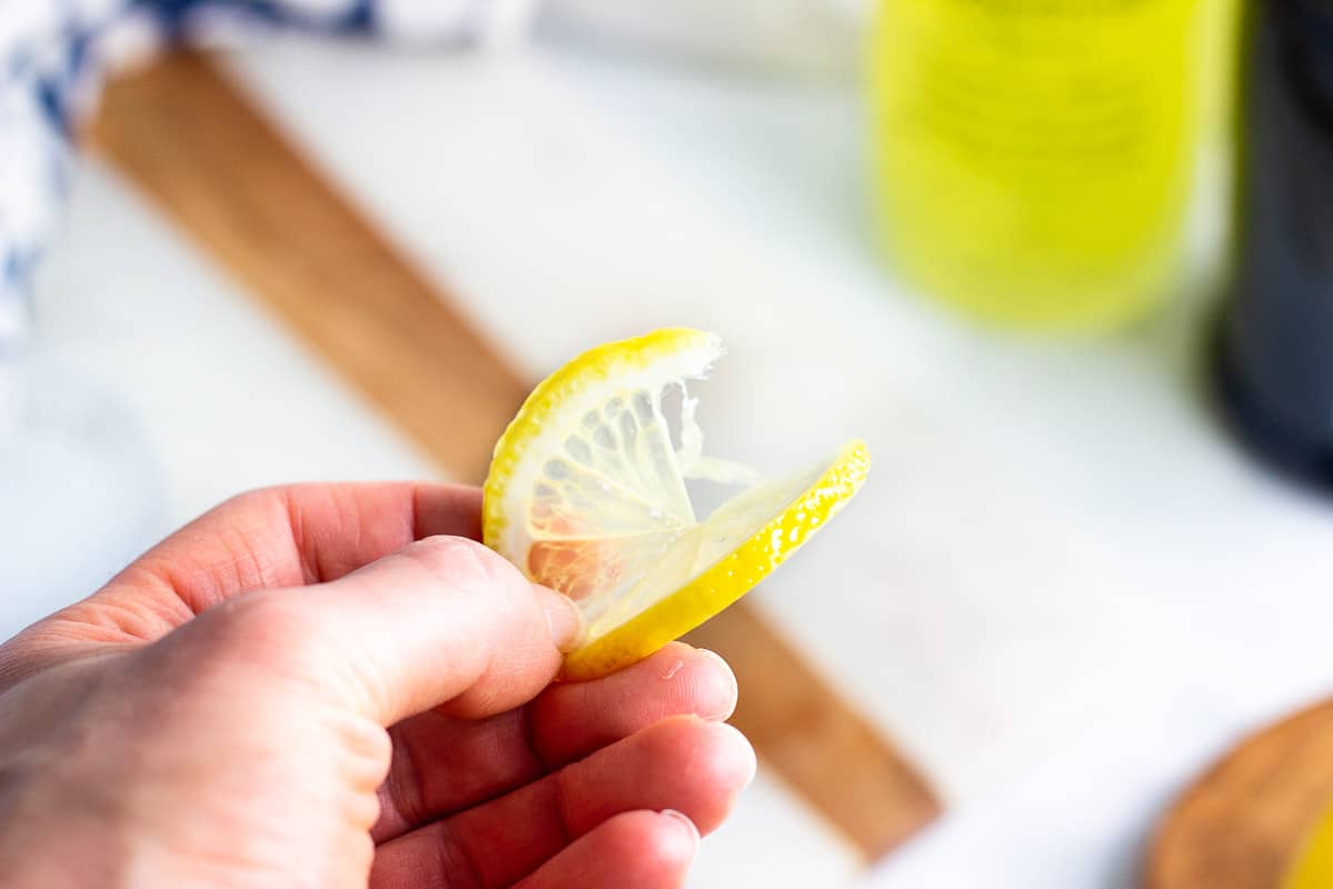 A hand holding a twisted lemon round for garnish.