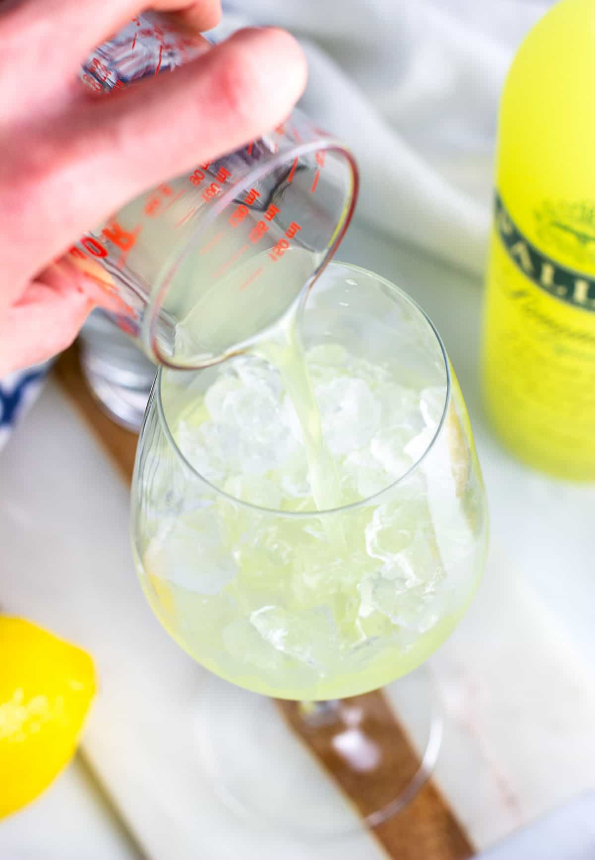 Limoncello being poured into a stemmed wine glass half filled with ice.