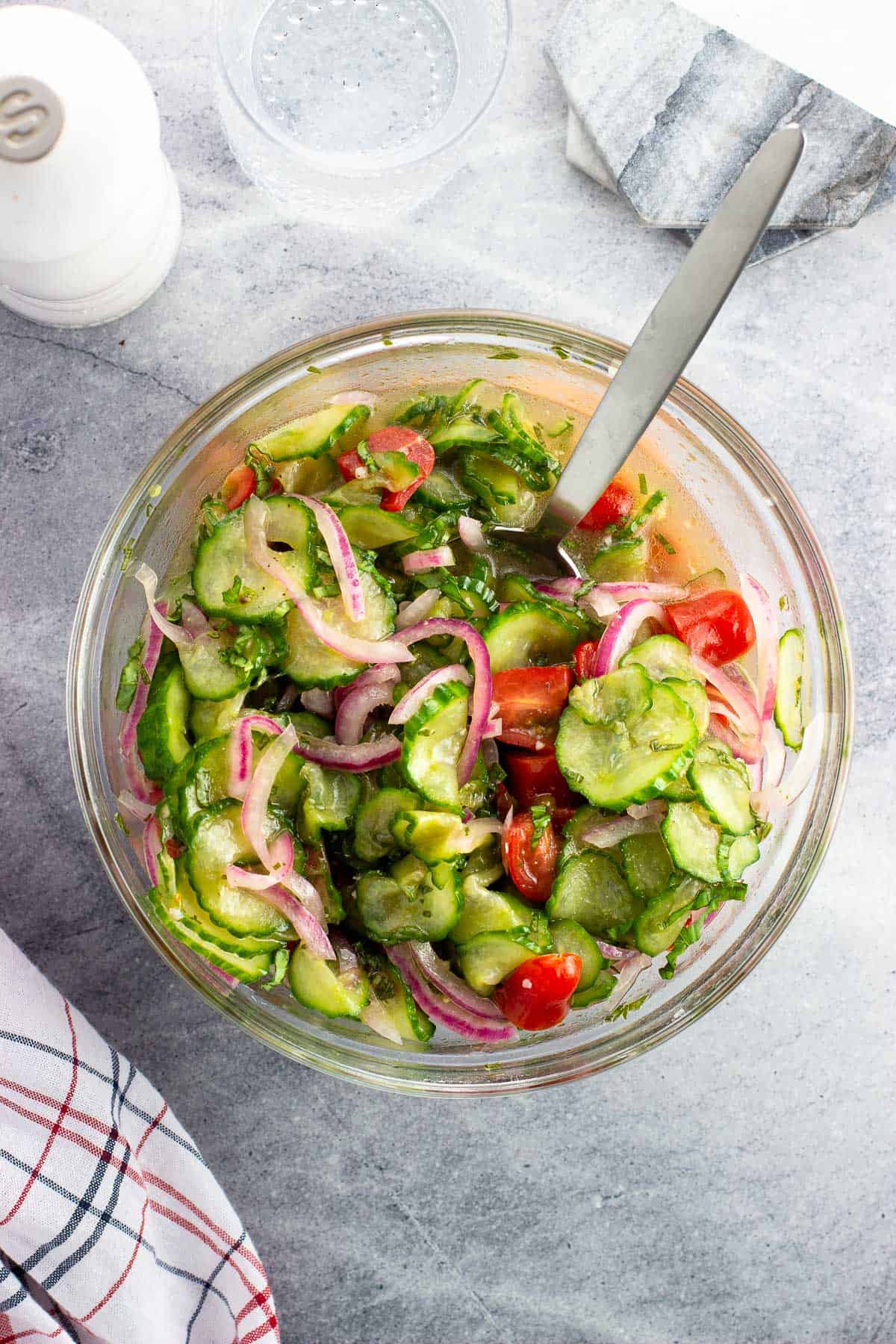 Cucumber, tomato, and red onion salad in a bowl with a serving spoon.