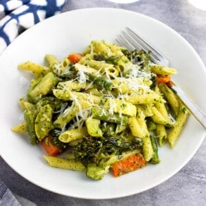 A shallow bowl of pesto pasta primavera with a fork.