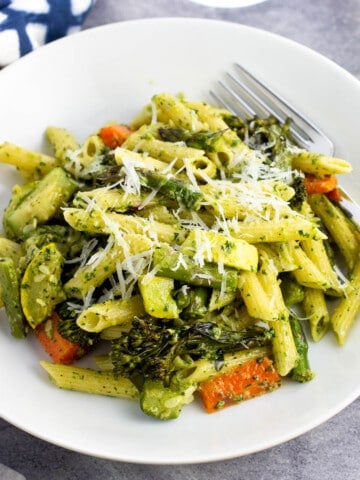 A shallow bowl of pesto pasta primavera with a fork.