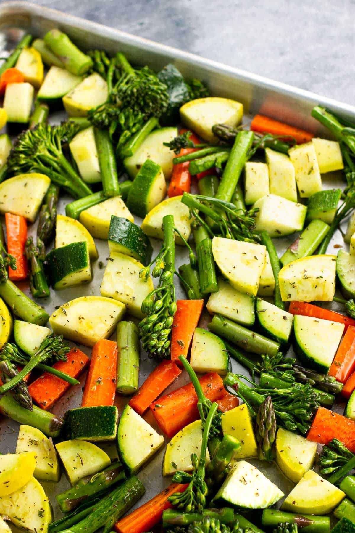 Raw chopped vegetables coated in oil on a sheet pan.