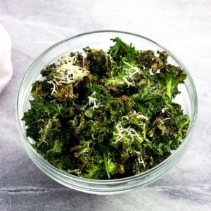 A bowl of kale chips, some coated in Parmesan.