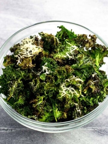 A bowl of kale chips, some coated in Parmesan.