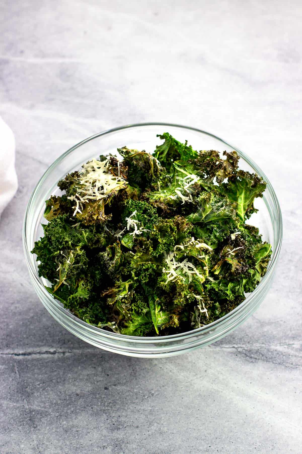 A bowl of kale chips, some coated in Parmesan.