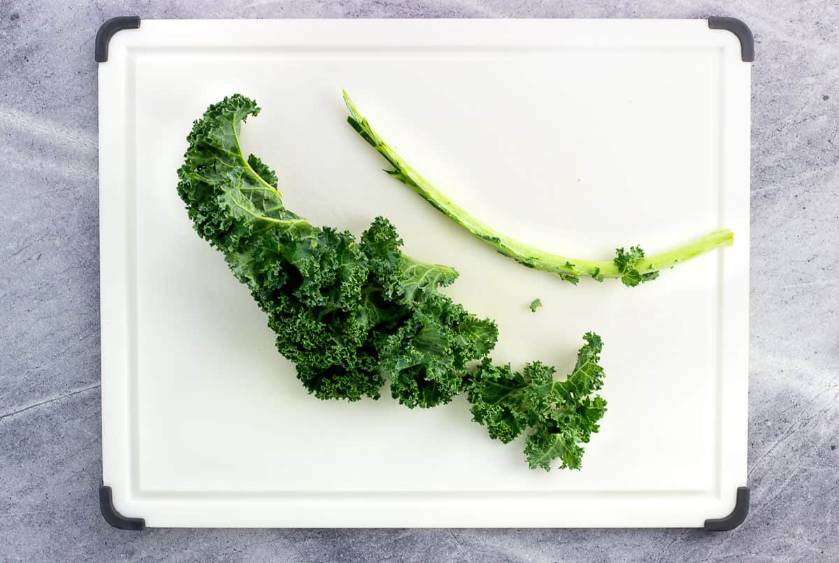 A kale leaf on a cutting board with the stem sliced off.